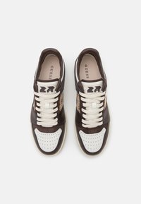 Sneaker atletiche marroni e bianche con accenti texturizzati, punta forata, lacci piatti e dettaglio del logo lateralmente.