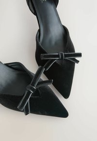 Czarne baleriny z zaostrzonym noskiem, z aksamitnymi kokardkami na górze, posiadają gładkie czarne wkładki i eleganckie detale przeszyć.