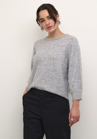 Lichtgrijze gebreide trui met een relaxed fit, ronde halslijn en driekwartmouwen. Gecombineerd met donkere broeken, met een zachte textuur.