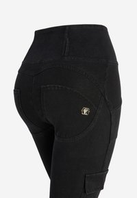 Jeans neri a vita alta con una superficie liscia, dettagli di cuciture curve e una piccola accentuazione in oro sul taschino posteriore.