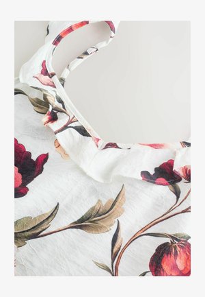 Balta gėlėta palaidinė su raukinėta iškirpte, ryškiomis raudonomis ir rožinėmis gėlėmis bei plonomis petnešėlėmis. Tekstūruota medžiaga su susiraukšlėjusia išvaizda.