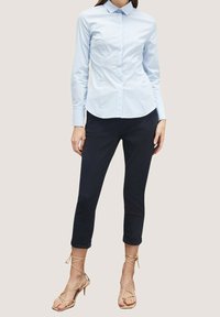 Camicia azzurra chiara a maniche lunghe con colletto abbinata a pantaloni neri cropped e sandali con tacco alto beige a fasce.