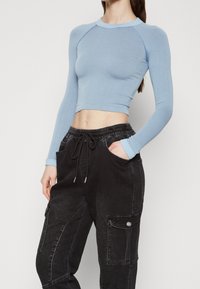 Světle modrý, dlouhý rukáv, žebrovaný crop top s kulatým výstřihem; v kombinaci s černými, volně padnoucími cargo kalhotami se bočními kapsami.