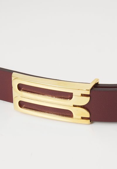Curea din piele burgundă, dotată cu o cataramă din metal auriu, cu două decupaje elongate și o suprafață texturată, oferind un design elegant și modern.