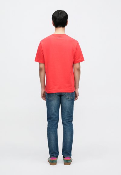 Κόκκινο βαμβακερό t-shirt με κλασικό στρογγυλό λαιμό, συνδυασμένο με μπλε τζιν παντελόνια και πολύχρωμα αθλητικά παπούτσια. Εμφανίζεται η πίσω όψη.