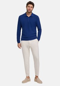 Niebieska polo z teksturą, z kołnierzykiem i trzema guzikami, połączona z białymi zwężającymi się spodniami i beżowymi butami typu slip-on.