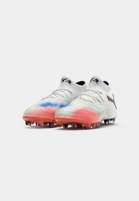 Witte voetbalschoenen met rode en blauwe verloopaccenten, zwart Puma-logo en enkelkousontwerp, zij aan zij gepositioneerd op een witte achtergrond.