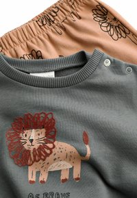Grå sweatshirt med et løvegraphic og teksten "Vær modig", parret med ferskenfarvede shorts med elastisk talje og blomsterdesign.