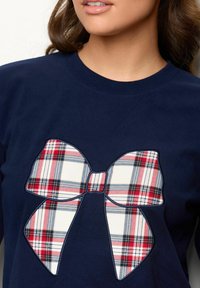 Navyblå sweatshirt med en stor, applikeret plaid sløjfe i hvid, rød og sort, med en glat tekstur og rund hals.