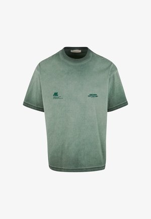 Zaļš kokvilnas T-krekls ar brīvu piegriezumu. Īsas piedurknes, apaļa kakla izgriezuma forma un tumši zaļi apdruka uz priekšpuses. Mīksta, strukturēta auduma.