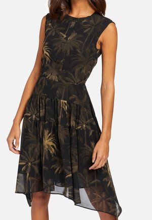 Vestido negro sin mangas con estampado marrón de palmeras, cintura ajustada y dobladillo asimétrico hasta la rodilla, usado por una mujer de pie.