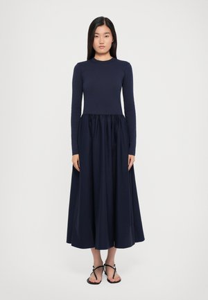 Vestido de manga larga azul marino con un corsé ajustado y una falda voluminosa y acampanada. Textura suave, de largo hasta el suelo, combinado con sandalias negras.