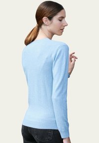 Pull à manches longues bleu clair en tissu doux. Il présente un col rond et une finition côtelée. Texture lisse avec des détails minimaux.