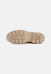 Beige gummiyttersåle med en teksturert, lug-mønster for grep. Rund form med definerte konturer og blomstermønstrete detaljer.