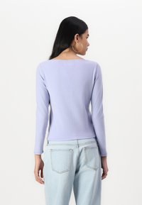 Lilac long-sleeve top made of soft fabric, featuring a simple round neckline and fitted design, paired with light blue jeans.
