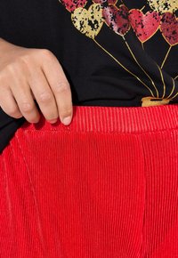 Rode ribfluwelen broek met een gestructureerde tailleband, gecombineerd met een zwart t-shirt met kleurrijke hartballonafbeeldingen.