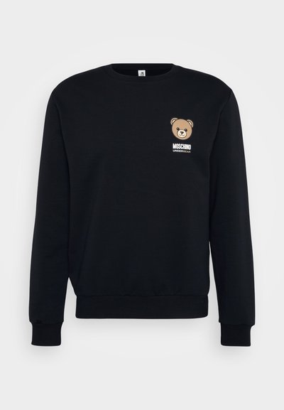 Mustat collegepaidat, jotka on valmistettu puuvillasta, sisältävät karhun graafisen kuvan vasemmassa rinnassa ja valkoisen tekstin "MOSCHINO UNDERBEAR" sen alla.