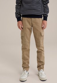 Beiga cargo-byxor med två sidofickor och en smal passform. Bärs tillsammans med en marinblå randig sweatshirt och vita sneakers.