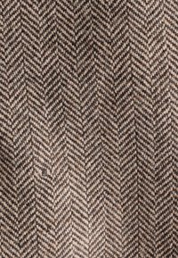 Tissu en laine marron et beige à motif chevrons, présentant des rayures en zigzag diagonales étroitement tissées.