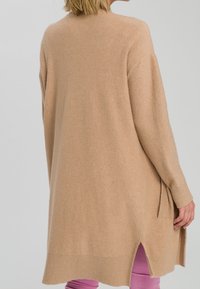 Cardigan in maglia beige con una vestibilità ampia, fessure laterali, polsini e orlo a coste, caratterizzato da una texture morbida e un retro leggermente allungato.