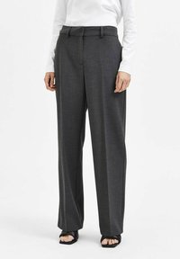 Pantaloni grigi su misura con design a gamba dritta, realizzati in un tessuto texturizzato, dotati di passanti per cintura e una piega frontale. Indossati con una maglietta bianca.
