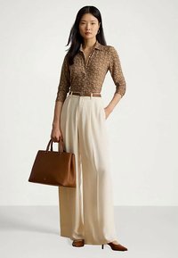 Brunmønstret langermet topp, kremfargede vide bukser, brun lærveske og spisse hæler. Har en knappet krage og belte.