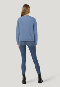 Hellblauer Pullover mit lockerer Passform, geripptem Saum und langen Ärmeln, kombiniert mit dunklen Skinny-Jeans und schwarzen Knöchelschuhen.
