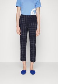 Marinblå rutiga byxor som slutar vid anklarna med en tajt passform, med ett rutig mönster i ljusblått. Matchas med en blå t-shirt och blå skor.