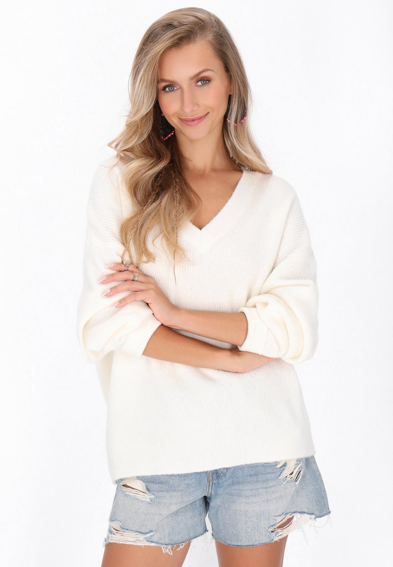 Pulover tricotat crem cu decolteu în V și umeri căzuți, asortat cu pantaloni scurți din denim cu aspect uzat. Textură ușoară și croială lejeră.