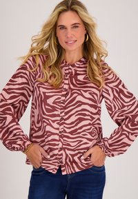 Lange mouwen blouse in een roze en bordeauxrood zebrapatroon, met een knoopsluiting aan de voorkant en elastische manchetten. De stof lijkt glad en licht van gewicht.
