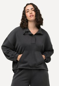 Wciągany sweter w kolorze węgla z półzamkiem, przednią kieszenią, długimi rękawami z elastycznymi mankietami oraz luźnym krojem. Gładka tekstura materiału.