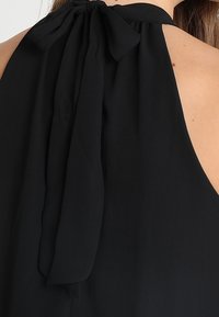 Czarny top na halter z dużą kokardą z tyłu, gładki materiał i otwarty tył, podkreślający smukłą sylwetkę.