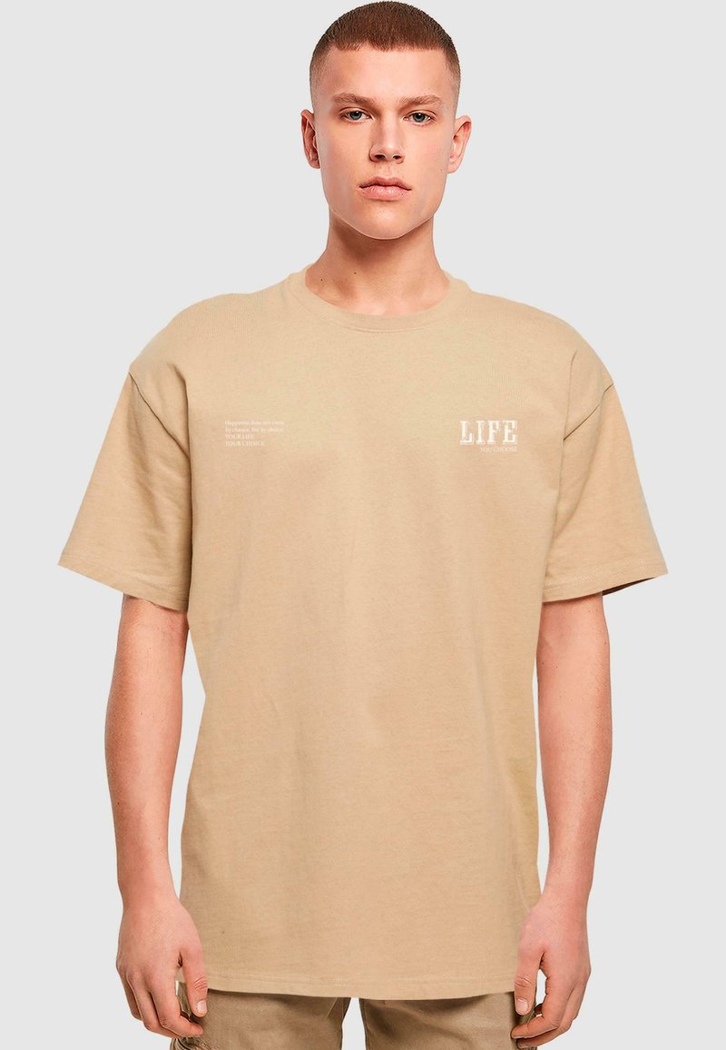 Beige bomulds t-shirt med løs pasform, korte ærmer, rund halsudskæring og fronttryk i hvid. Teksten inkluderer ordet "LIFE."