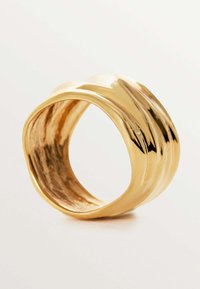 Anillo de metal dorado con un diseño liso y ondulado que presenta ranuras horizontales. El interior tiene un acabado pulido.