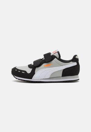 Zapatilla Puma en blanco y negro con dos correas de velcro negras, una franja lateral blanca, logo Puma naranja y suela negra sobre fondo gris.