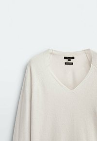 Pull en V blanc fabriqué en 100% cachemire, avec des bords côtelés et des manches raglan, texture douce avec un design simple et épuré.