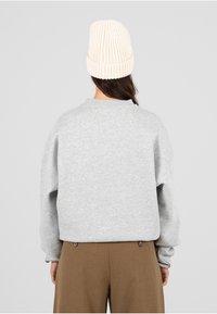 Grijze cropped sweatshirt met een ronde halslijn en verlaagde schouders, gecombineerd met bruine, hooggelegde broeken. Licht gebreide crèmekleurige beanie op het hoofd.