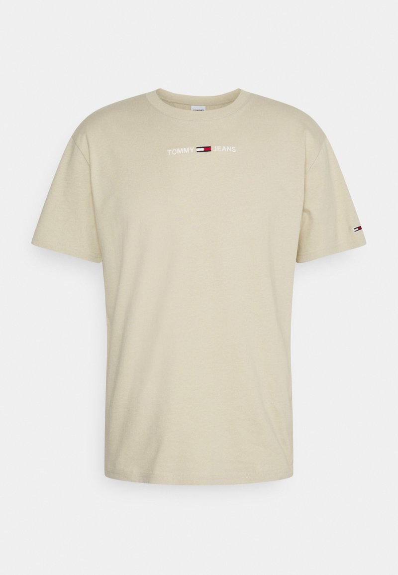 Světle béžové bavlněné tričko s krátkým rukávem, s potiskem loga "TOMMY JEANS" v bílé barvě a červeno-modrou nášivkou na levém rukávu.