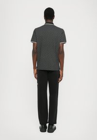 Polo noir à motifs avec un col et des manches courtes, associé à un pantalon noir ample et des chaussures à plateforme noires, vu de dos.