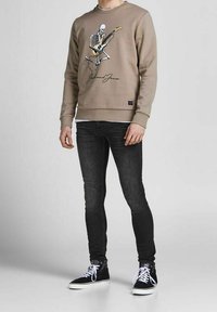 Sudadera beige con un gráfico de un esqueleto tocando la guitarra, combinada con jeans ajustados negros y zapatillas altas negras con cordones blancos.