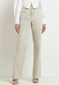 Jeans de pierna ancha beige con talle alto, que cuentan con una textura sutil, bolsillos frontales y dobladillos sin terminar. Combinados con una blusa corta blanca.