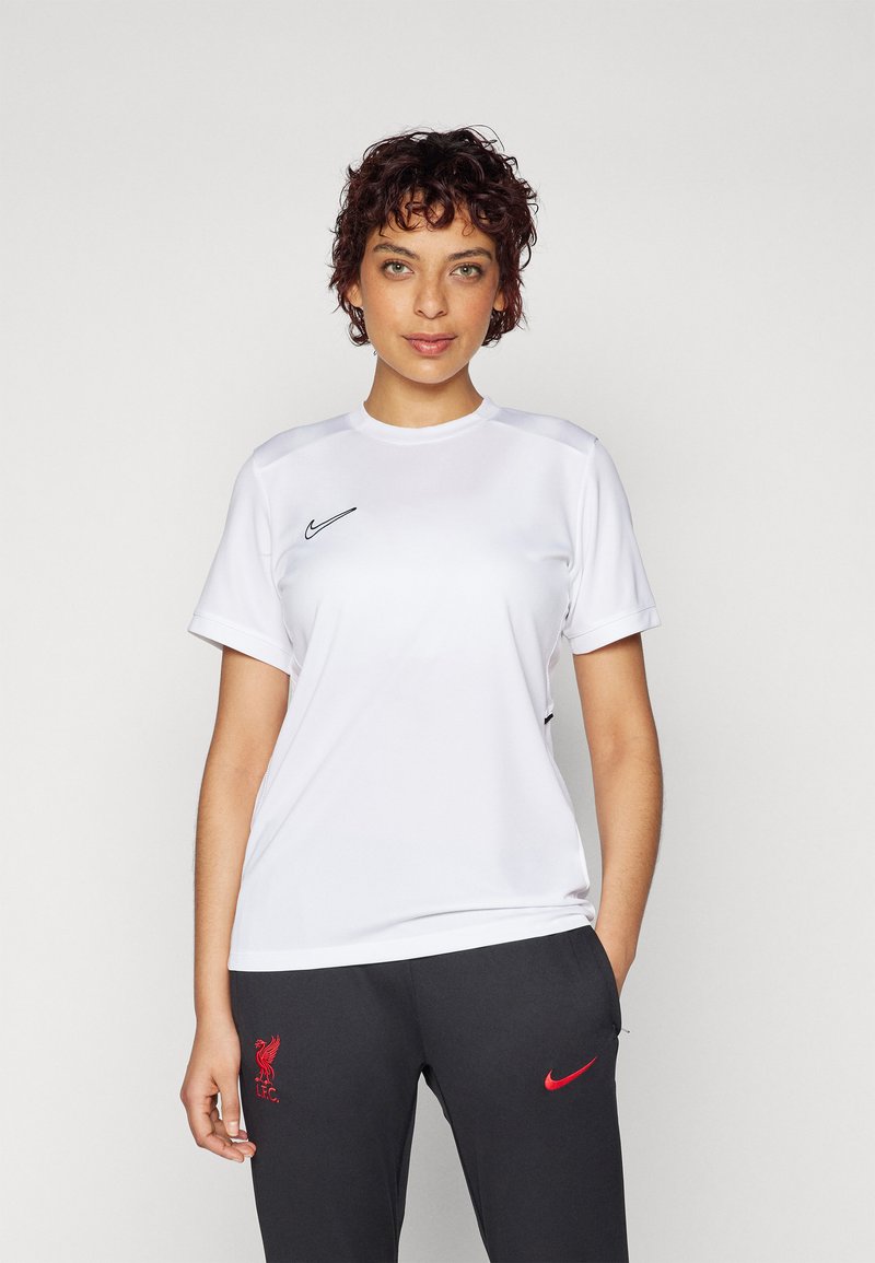 Biela atletická športová tričko s krátkym rukávom, okrúhlym výstrihom a čiernym logom Nike na hrudi, kombinované s tmavošedými nohavicami s červeným logom.