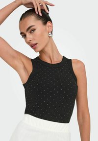Zwarte geribde tanktop met zilveren stippenversieringen, ronde halslijn en mouwloos ontwerp, gecombineerd met een gelaagde witte rok.