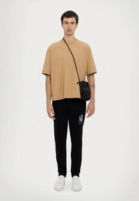 Camiseta beige de gran tamaño, pantalones jogger negros con logo, bolso bandolera negro, zapatillas blancas; textura suave, ajuste relajado, estilo casual moderno.