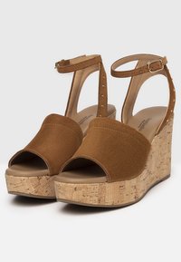 Braune Wildleder-Wedge-Sandalen mit offener Zehe, Korkplattform, Knöchelriemen und goldenen Nietenakzenten am Riemen.