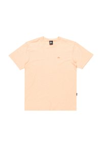 Camiseta de manga corta color melocotón claro, fabricada en tejido suave. Presenta un pequeño logo en el centro y una etiqueta en el lado izquierdo cerca del dobladillo.