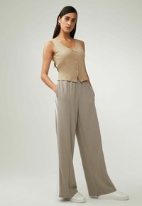 Top sin mangas de canalé beige con botones en la parte delantera y pantalones de pierna ancha grises que presentan bolsillos laterales y franjas blancas de acento.