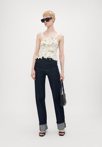 Blomstrete peplum-topp med hvit bunn, mørkeblå høy midje jeans og svarte tilbehør, inkludert store solbriller og en veske.