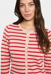 Napapaita vaaleanpunaisena, jossa on leveät punaiset raidat. Ominaisuuksiin kuuluu pyöreä pääntie ja kuusi etunappia. Pehmeä, neulottu rakenne.