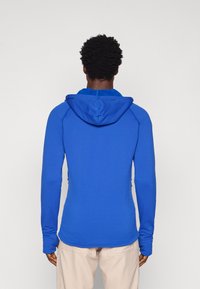 Sudadera azul de manga larga fabricada con tejido elástico. Presenta un diseño ajustado, capucha y puños con orificios para los pulgares. Textura suave sin patrones.